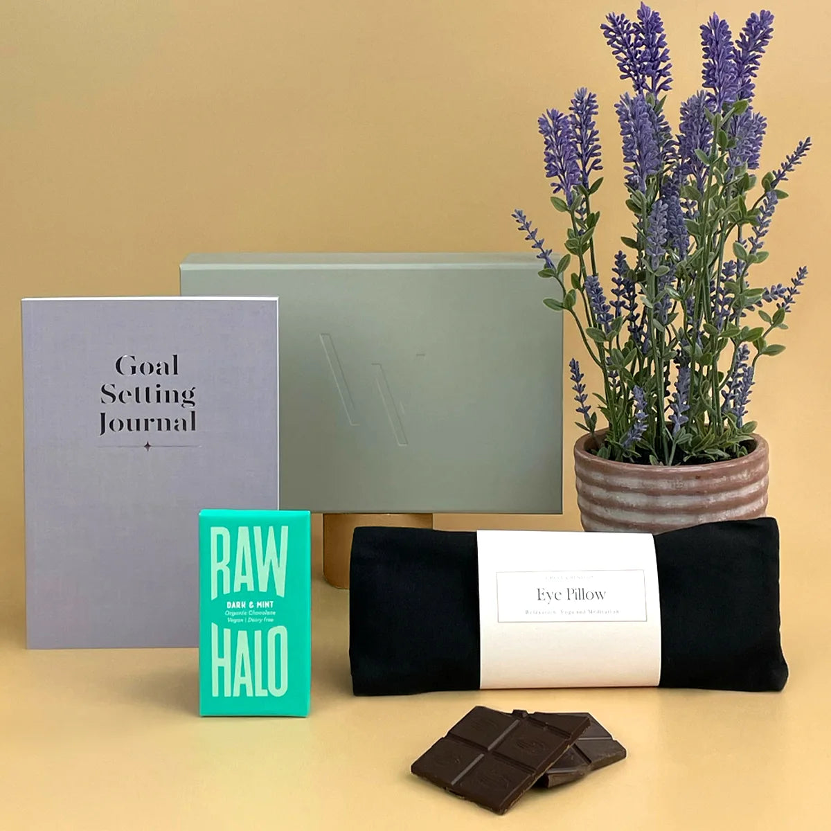 Selfcare Gift - Goal setting journal, raw halo product, eye pillow, chocolate, and lavender plant on a beige background