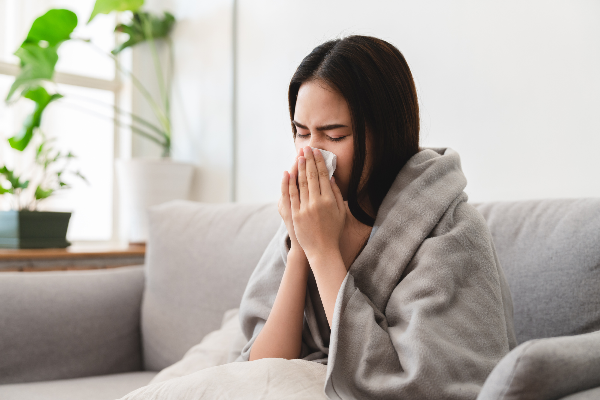 Unwell lady blowing nose in a blanket.